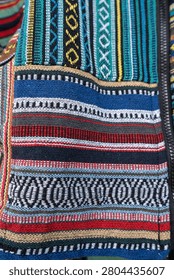 close up texture of fabric pattern multi-colored traditional handwoven Southeast Asian hill tribe textile art paneled patchwork layout with complex geometric borders, diamonds, and linear stripes woven directly into a heavy, tactile cotton canvas.teal electric blue canary yellow crimson red set against deep indigo black and neutral sand tones bg