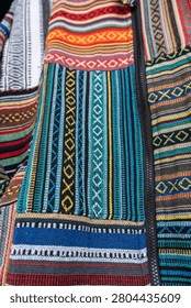 close up texture of fabric pattern multi-colored traditional handwoven Southeast Asian hill tribe textile art paneled patchwork layout with complex geometric borders, diamonds, and linear stripes woven directly into a heavy, tactile cotton canvas.teal electric blue canary yellow crimson red set against deep indigo black and neutral sand tones bg
