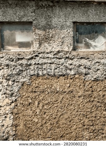Close up texture of an old weathered roughcast plaster wall with peeling section revealing earthen clay underneath and two small square windows