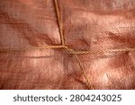 Close up texture of an orange woven plastic tarp secured tightly with crossing brown nylon ropes