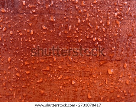 Close up texture of reddish wood surface with water droplets. Wet wooden background with rain drops pattern for natural wallpaper.