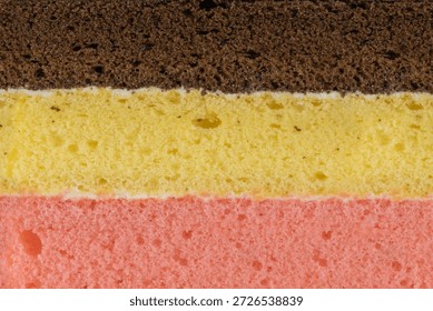 Close up texture of a three layered sponge cake with chocolate, vanilla, and strawberry flavors. Macro background of colorful porous steamed cake layers. 