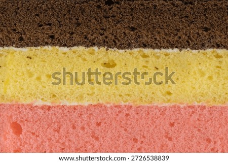 Close up texture of a three layered sponge cake with chocolate, vanilla, and strawberry flavors. Macro background of colorful porous steamed cake layers. 