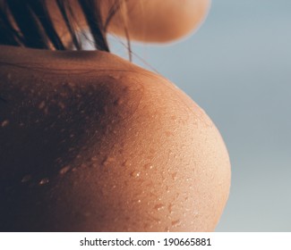 Close Up Texture Of The Wet Shoulder Of A Young Woman Showing Skin Detail And The Way The Water Condenses And Beads On The Surface Of The Skin Against A Sunny Blue Summer Sky