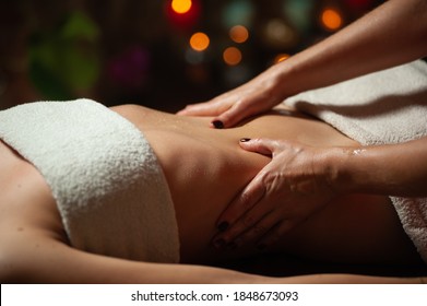 Close Up Of Therapist Doing Stomach Massage On Woman In Spa Against Dark Background.