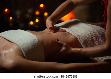 Close Up Of Therapist Doing Stomach Massage On Woman In Spa Against Dark Background.