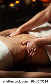 Close Up Of Therapist Doing Stomach Massage On Woman In Spa Against Dark Background.