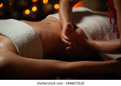 Close Up Of Therapist Doing Stomach Massage On Woman In Spa Against Dark Background.