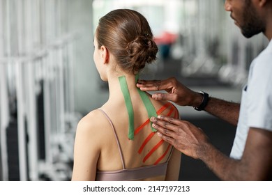 Close up of therapist putting kinesio tape on back and shoulder of young woman in physiotherapy session