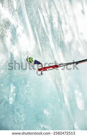 Close up thin quickdraw with red climbing carabiner hooked the ring ice screws screwed into the ice of a frozen glacier wall. Concept of climber gear