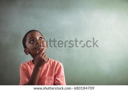 Close up of thoughtful boy standing against greenboard in classroom