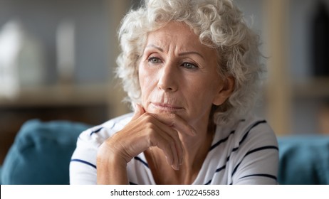 Close Up Thoughtful Mature Woman Worried About Problems, Looking Into Distance, Touching Chin, Upset Pensive Older Senior Female Sitting On Couch At Home Alone, Loneliness And Depression