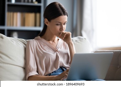Close up thoughtful upset woman looking at laptop screen, pondering ideas or difficult tasks, sitting on couch at home, pensive young female touching chin, reading news, waiting for message