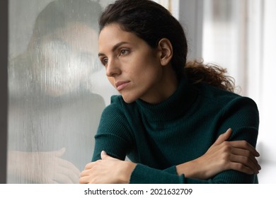 Close up thoughtful upset woman looking in rainy window alone, lost in thoughts, pensive unhappy young female feeling lonely and depressed, thinking about relationship or personal problems