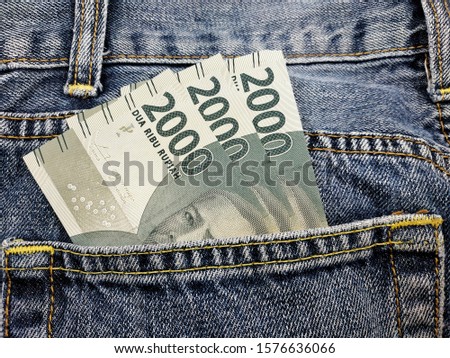close up three bills of two thousand rupiah in the back pocket of jeans