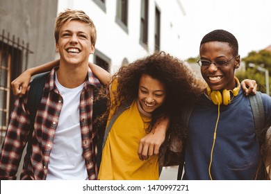 Close up of three college friends standing in the street with arms around each other. Cheerful boys and a girl wearing college bags having fun walking outdoors. - Powered by Shutterstock