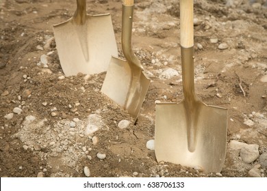 Close Up Of Three Gold Painted Shovel Heads Dug Into Sand And Rock Dirt At Ceremonial Ground Breaking Event For Commercial And Residential Building Development