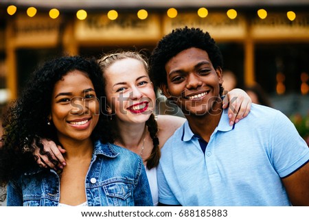 Close up of three multiethnic hipster teenagers friends laughing and hugging while spending time together outdoor over pub or cafe background.