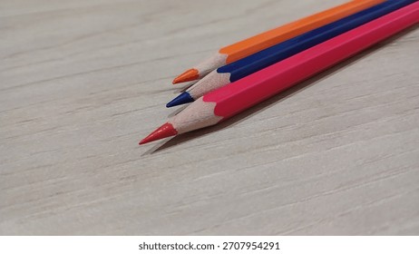 Close up of three sharp colored pencils lying diagonally on a light wooden texture background with copy space