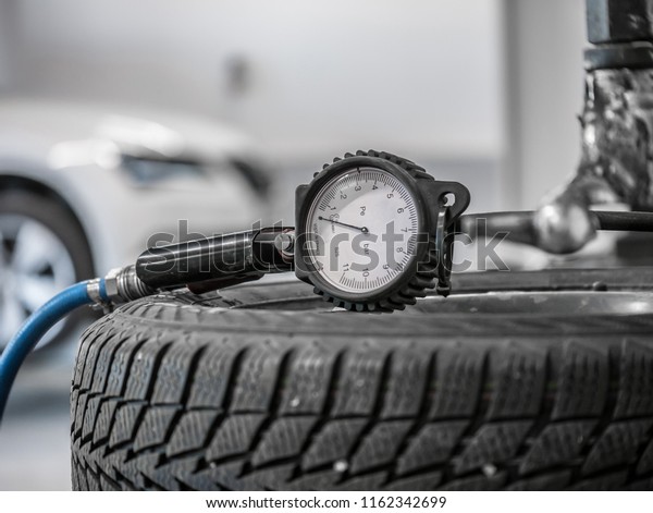 Close up tire and checking\
air pressure with gauge pressure in service station. Tire pressure\
gauge on the wheel. White car in background. Tire pressure gauge\
closeup.