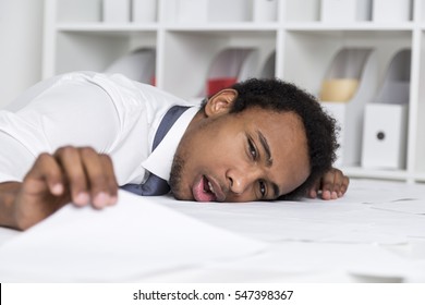 Close up of a tired African American clerk who has laid his head on a table and holding a document. Concept of too much paperwork.
