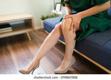 Close up of a tired woman legs with a dress on high heels while resting on the couch. Caucasian woman with an injury rubbing her knee 