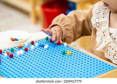 Close Up Toddler Girl's Hands Playing With Montessori Peg Board Wooden Material Practicing Fine Motor Skills