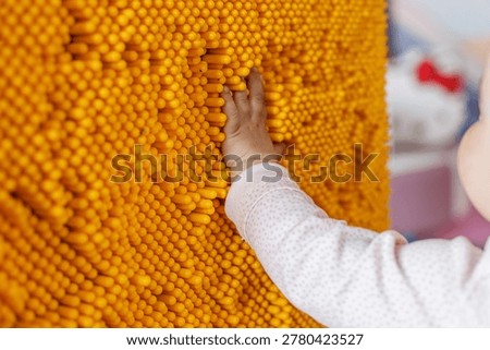 Close up of toddler hand touching interactive sensory wall in indoor play center. Authentic childhood activity focused on tactile exploration, sensory learning and development.