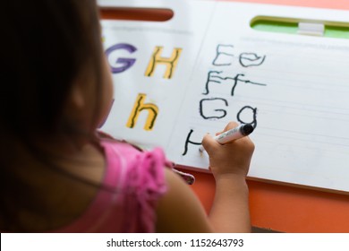 Close Up Of A Toddler Learning How To Write The Abcs On Her Desk, In Classroom.