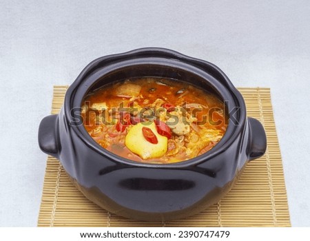 Close up of Tofu Stew with soft tofu, egg and red peppers on earthen pot and sushi roller mat, South Korea
