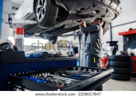 Close up of a tools in a drawer on toolbox with worker repairing car in blurry background at mechanic's shop.