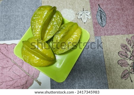 close up top shot of three green starfruit on a green plate on a table with table cloth