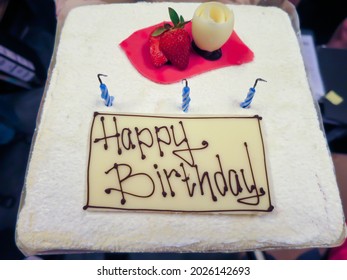 Close Up Top View Of Birthday Cake With White Icing, Sliced Strawberry And Candles On Table. Bokeh Background. No People.