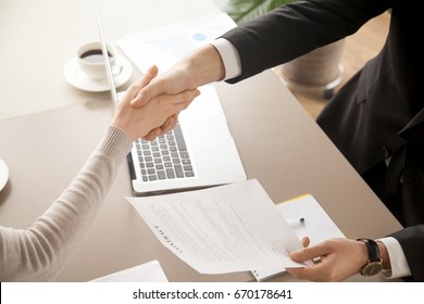 Close up top view of business handshake, male and female hands shaking over office desk after signing contract, holding signed statement, sealing deal as good result of successful negotiations  - Powered by Shutterstock