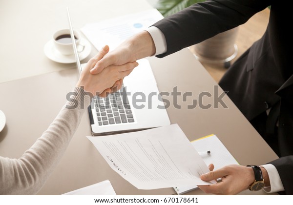Close up top view of business handshake, male and female\
hands shaking over office desk after signing contract, holding\
signed statement, sealing deal as good result of successful\
negotiations 