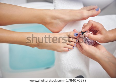 Close up top view of female having her toe nails painted by beautician in spa salon