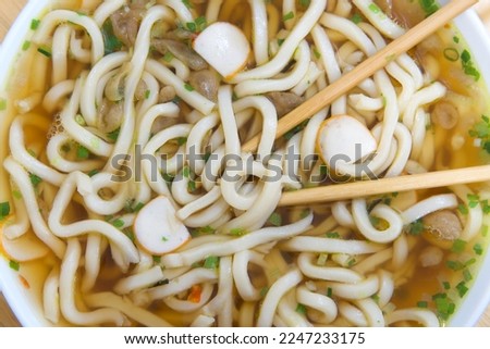 Close up top view flat lay of one bowl of udon noodles in beef broth. Chop sticks in bowl.