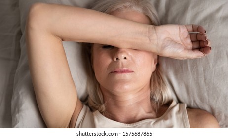 Close up top view middle-aged woman lying down in bed on pillow put hand on face, concept of female having insomnia sleeping disorder or migraine pain, melancholic mood, personal life troubles concept - Powered by Shutterstock