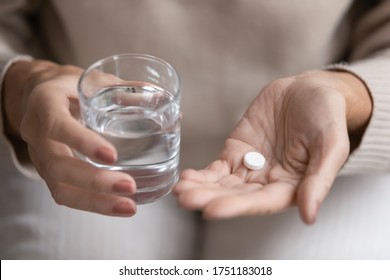 Close up top view of older woman hold glass of water and antibiotic aspirin pill feel unhealthy at home, sick mature female take daily dose of supplements or vitamins, elderly healthcare concept