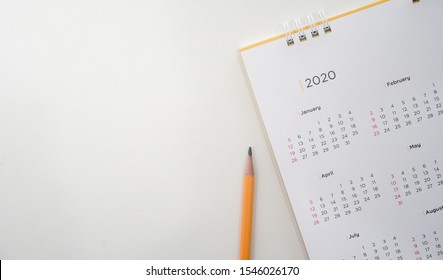 close up top view on white calendar 2020 with yellow pencil and month schedule to make appointment meeting or manage timetable each day lay on brown wood table background for planning work and life