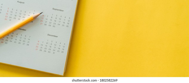 Nahaufnahme der Draufsicht auf weißem Kalender mit Bleistift und Monatsplan, um Termintreffen zu treffen oder Stundenplan zu verwalten jeden Tag auf gelbem panoramischem Hintergrund für die Planung von Arbeit und Lebenskonzept