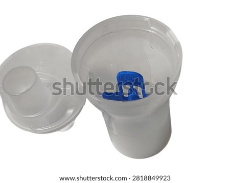 A close up top view of an open transparent plastic nebulizer medicine cup containing a blue baffle piece, with its cap placed beside it, isolated against a white background.
