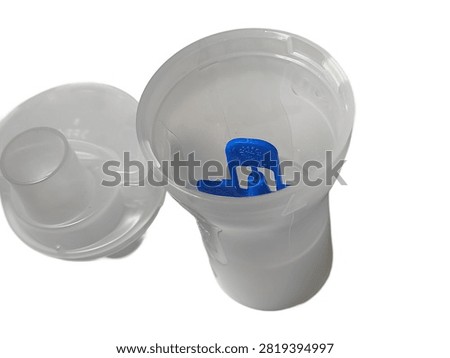 A close up top view of an open transparent plastic nebulizer medicine cup containing a blue baffle piece, with its cap placed beside it, isolated against a white background.