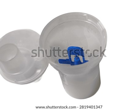 A close up top view of an open transparent plastic nebulizer medicine cup containing a blue baffle piece, with its cap placed beside it, isolated against a white background.