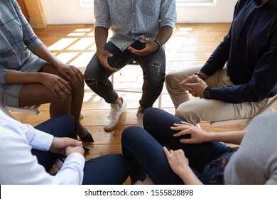 Close up top view unrecognizable multiracial workers strategizing indoors at informal atmosphere, people seated in circle talking share problems tell stories during psychological rehab session concept