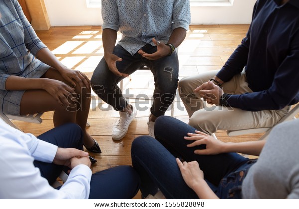 Close up top view unrecognizable multiracial
workers strategizing indoors at informal atmosphere, people seated
in circle talking share problems tell stories during psychological
rehab session concept