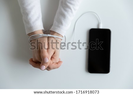 Close up top view of woman hands connected with wire cable to smartphone gadget, female bound addicted to cellphone device, dependent on social media, internet technology, addiction concept