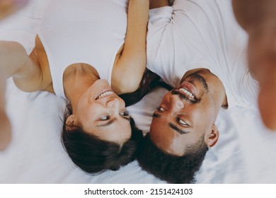 Close up top view young couple two man woman family in casual white clothes lying in bed do selfie shot pov on mobile phone look at each other spend time together in bedroom lounge home house wake up