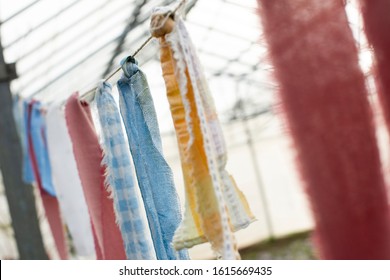 Close Up Of Torn Fabric Strips Tied To A Wire With Greenhouse In The Background