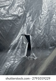 Close up of torn transparent plastic sheet with wrinkles and textured surface, creating an abstract background with a small opening in the center.